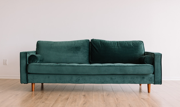 A dark green velvet sofa with wooden legs, set against a white wall.