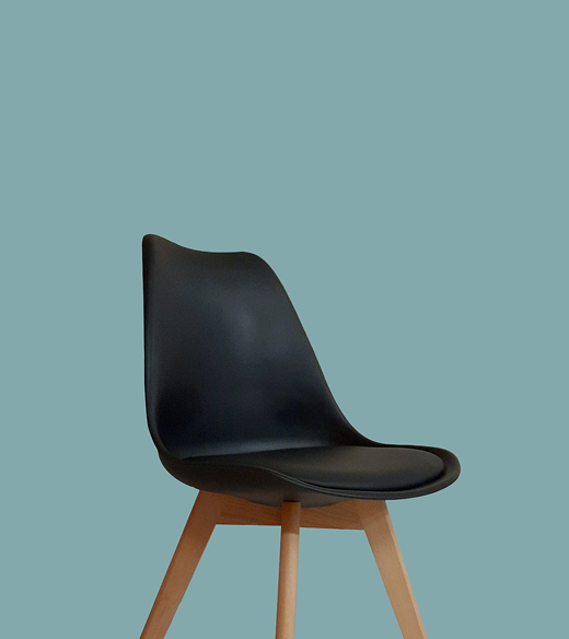 A contemporary dark chair with a curved back and wooden legs, set against a light blue wall.